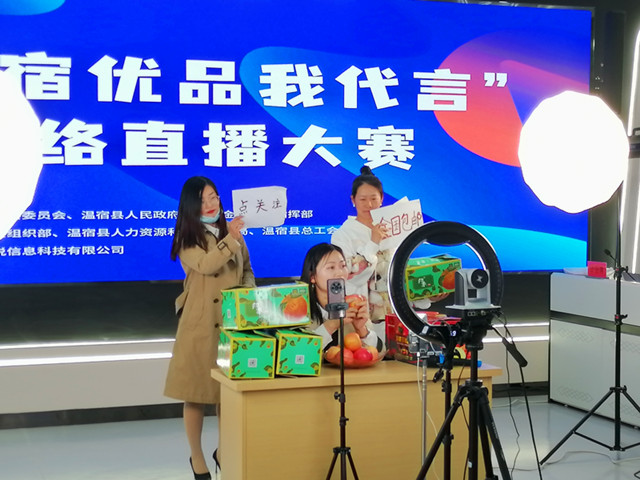 ‘温宿优品’网络直播大赛参赛选手何敏边对着手机端着自家种植的冰糖心苹果展示并开展试吃（江凯摄）_副本.jpg